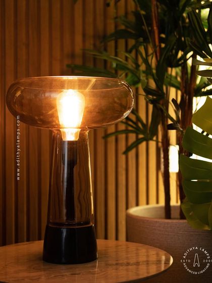 This simple and elegant table lamp features a warm filament bulb within a smoked glass shade. It's a perfect companion for a side table, providing a cozy and inviting ambient light for any corner.