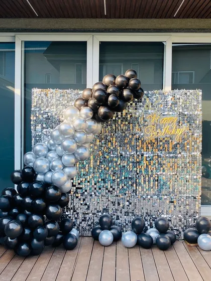 A poolside birthday party with a black and silver theme, featuring a shimmer wall and balloon garland.