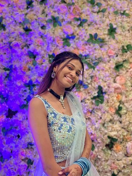 A happy client wearing a light blue floral embroidered blouse with a matching pre-draped saree. It's a fresh and pretty look, perfect for a daytime event.