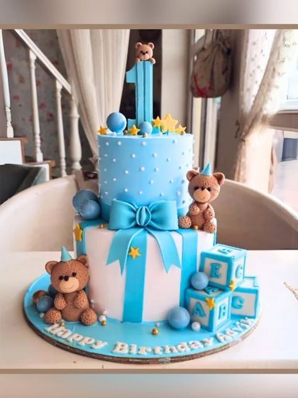 A sweet two-tier first birthday cake in blue and white, decorated with cute teddy bears and alphabet blocks.