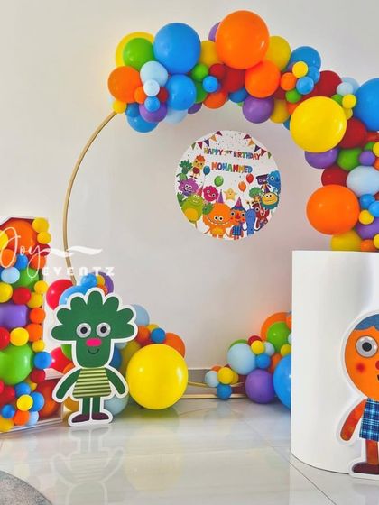Here is another Super Simple Songs theme, designed around a circular balloon arch. The decoration includes a large, balloon-filled marquee number '1', character cutouts, and a custom printed sign for the birthday boy.