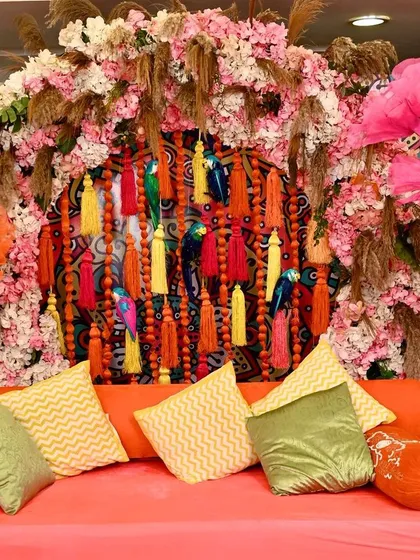 A close-up of the Mehendi decor, showing the mix of textures from the tassels, flowers, and the printed backdrop.