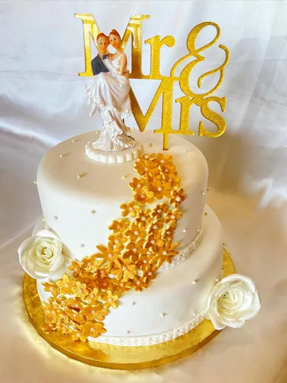 This two-tier wedding cake was based on a client's inspiration photo, which I elevated into a unique masterpiece. It features a cascade of golden sugar flowers, white roses, and a classic bride and groom topper.