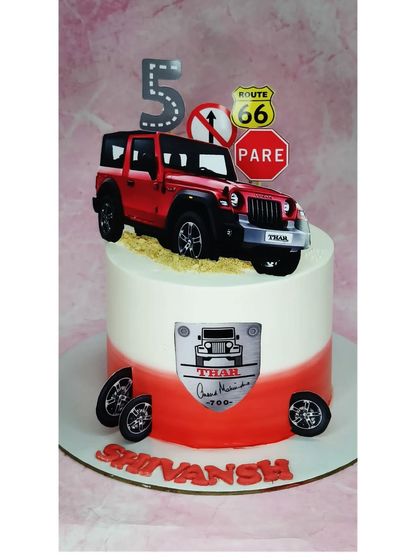 A cake for a Thar enthusiast's 5th birthday. This tall choco-chip cake features a red Thar jeep, road signs, and edible dirt for an off-roading adventure.