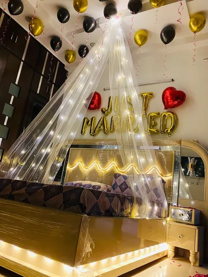 The reflection in the mirrored wardrobe shows the full effect of the black and gold balloons and the glowing canopy in this wedding night setup.