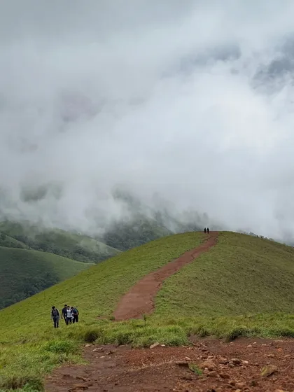 A group of trekkers on a distant ridge, dwarfed by the scale of the Netravathi landscape. It shows the true grandeur of the Western Ghats.