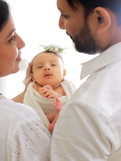 A close-up family portrait where the parents are looking at each other, with their baby held lovingly between them. The focus is on the shared joy and love in their expressions.