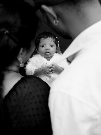 A powerful black and white photo capturing the first moments with a newborn. The focus is on the baby's curious eyes, framed by the loving parents.