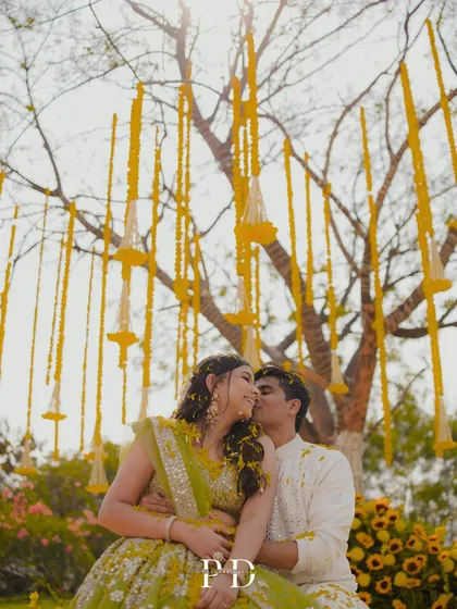 A romantic moment for the couple during their sunflower Haldi. The hanging marigold garlands create a beautiful, dreamy filter for their portraits.
