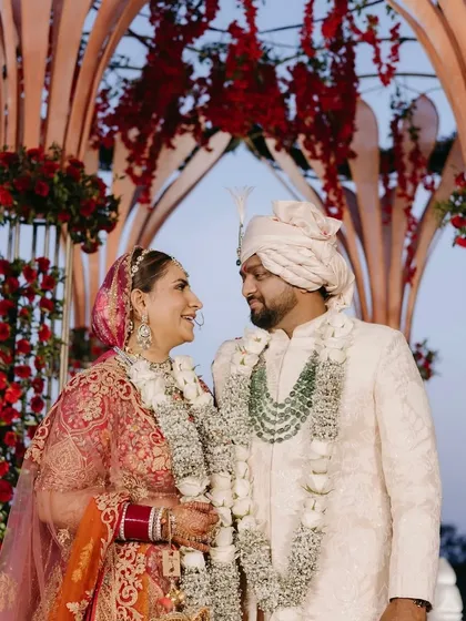 A close-up of the couple at their royal Goa wedding. The grand, lotus-petal-shaped mandap is adorned with rich red flowers, creating a regal and romantic frame.