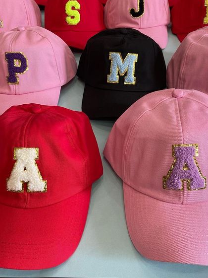 A vibrant assortment of personalized initial caps in pink, red, and black. These make for fantastic and memorable return gifts for kids' birthday parties.