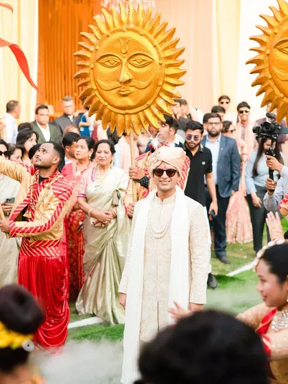 The groom's arrival is a statement. Here, he enters amidst a cloud of smoke, flanked by dancers and attendants with sun props, creating a powerful and photogenic moment that captures his royal arrival.