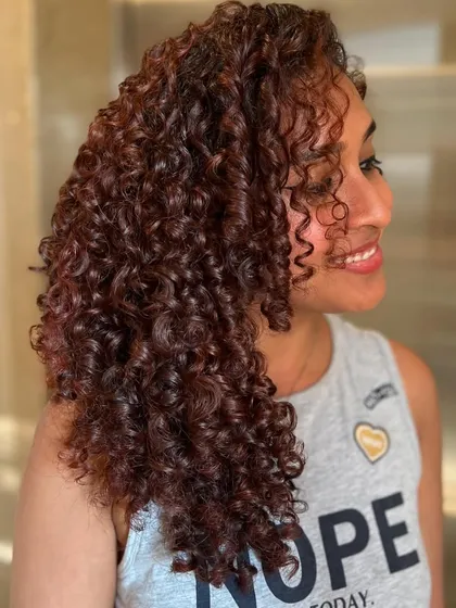 A happy client showing off her Pumpkin Spice curls. The color complements her skin tone beautifully and her curls are defined and frizz-free.