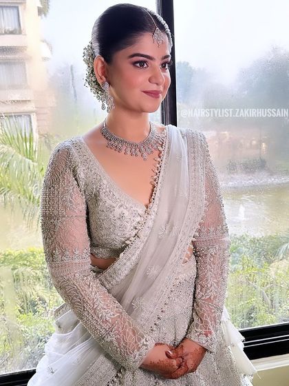 A beautiful morning bride with a sleek, center-parted bun. The look is completed with baby's breath and modern gold accessories for a chic and minimalist feel.