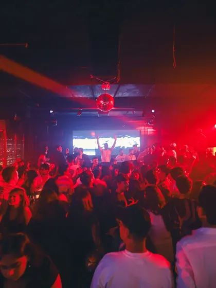 A wide shot of the packed house at Ark Lounge. The red haze and silhouettes of the crowd create a classic club scene.