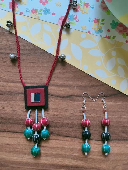 This necklace set features a fabric pendant with colorful thread-wrapped beads. The matching long earrings complete the look, making it an easy choice for Durga Puja or Navratri celebrations.