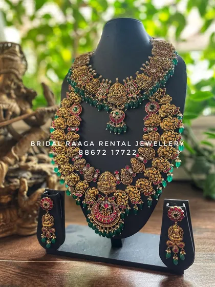 A grand bridal set with heavy carvings and green bead accents. The choker and haram both feature prominent Lakshmi motifs.