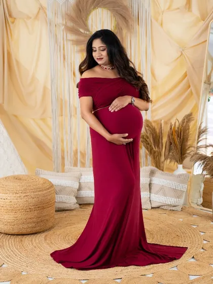 A full-length portrait of a mom-to-be in a beautiful deep red gown. The simple elegance of the dress is highlighted in our boho studio setting.