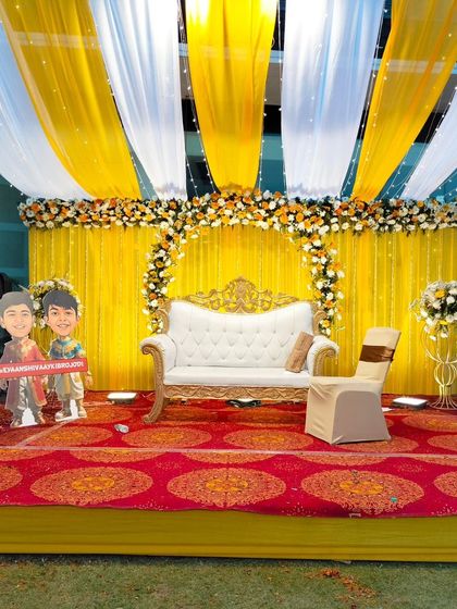 A fun and quirky Haldi stage setup with cartoon cutouts of the couple. The yellow and white drapes with floral accents create a cheerful and personalized atmosphere.