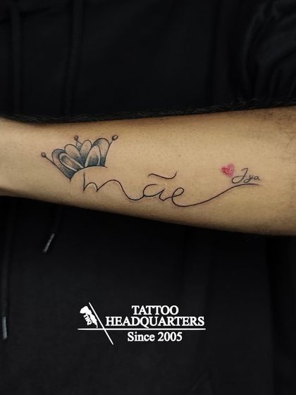 A tattoo that reads "mãe" (Portuguese for mom) with a crown, and "Jya" with a heart, a beautiful tribute to family.