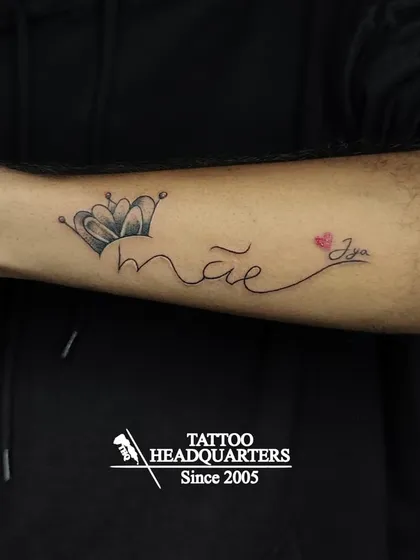 A tattoo that reads "mãe" (Portuguese for mom) with a crown, and "Jya" with a heart, a beautiful tribute to family.
