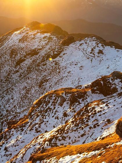 Another perspective of the sun-kissed mountains in Uttarakhand. This aerial shot showcases the layered ridges and the warm glow on the snow, capturing the immense and peaceful landscape from a unique angle.