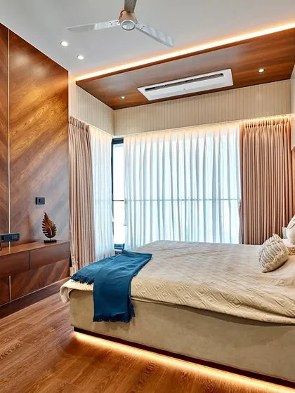 This bedroom is a study in warmth and texture. We used a chevron-patterned wood veneer for the wall paneling and a matching wooden false ceiling, complemented by soft, indirect lighting to create a cozy and inviting retreat.