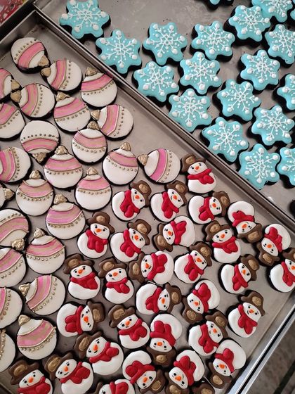 A tray full of my hand-decorated Christmas cookies. This assortment includes detailed snowman cookies, pink ornaments with gold accents, and delicate blue snowflakes, all piped with royal icing.