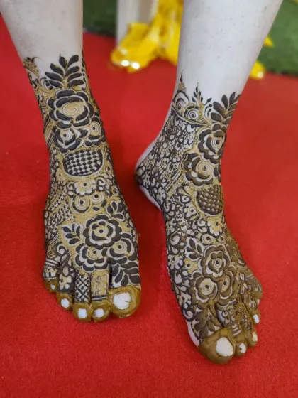 This design for the feet features a mix of floral patterns and checkerboard fills, with the toes fully covered in henna for a traditional finish.