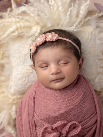 A sweet smile from a sleeping angel. The soft pink wrap and fluffy background create a dreamy and gentle portrait.