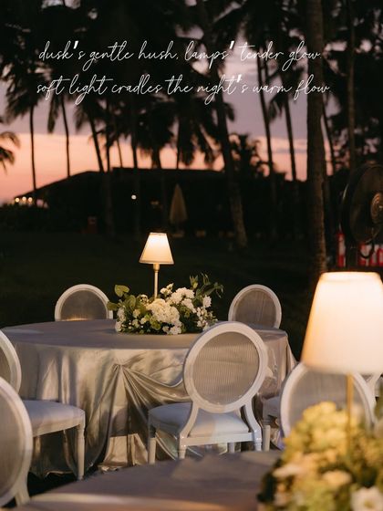 A table at the Goa soirée, with a beautiful floral centerpiece and elegant lamp lighting, set against the backdrop of the setting sun.