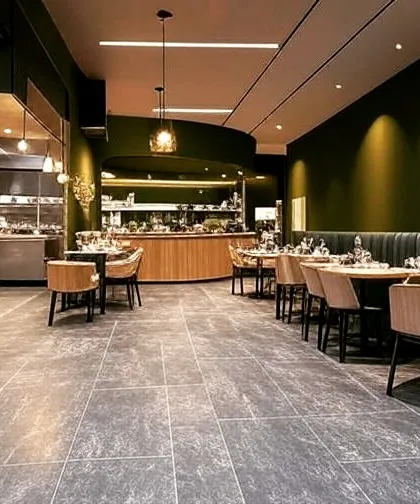 A modern restaurant design with an open kitchen concept. The olive green walls, dark flooring, and mix of booth and chair seating create a contemporary and dynamic dining space.