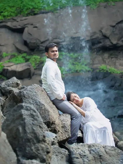 A creative and tender pose during a waterfall maternity session. The mother-to-be rests her head gently on her partner's leg, showcasing their comfortable intimacy and connection amidst the rugged, natural beauty of the location.