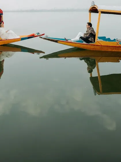 An artistic shot of two Shikara boats side-by-side on Dal Lake, creating a beautiful, symmetrical reflection in the water. This is a unique take on the classic Kashmir pre-wedding shoot.