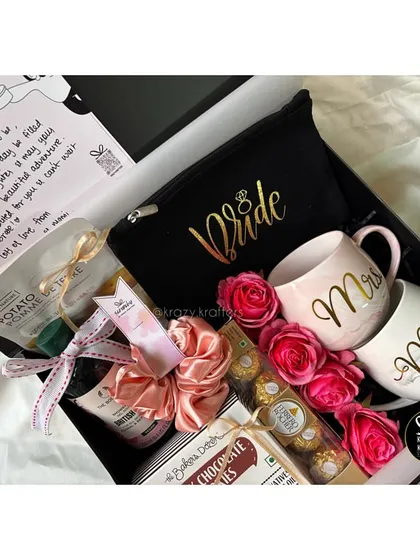 A beautiful 'Bride to Be' hamper featuring 'Mr' and 'Mrs' mugs, a personalized 'Bride' pouch, Ferrero Rocher, and other treats, all tied together with pink roses.