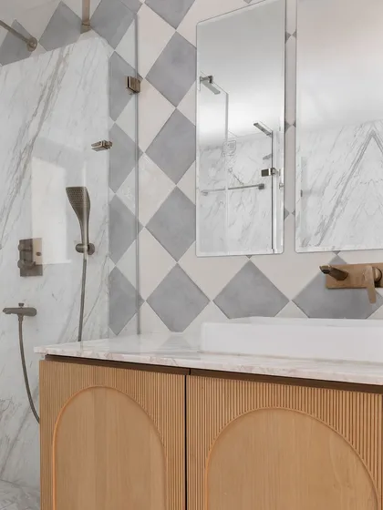 This elegant bathroom features a custom wood vanity with arched, reeded door panels. The walls are a mix of diamond-patterned marble tiles and a large marble slab, creating a rich, textural look.