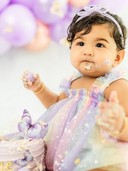A handful of cake and a world of wonder in her eyes. This is the essence of a first birthday celebration, captured in a single frame.