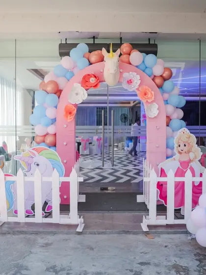 A sweet and charming Princess and Unicorn themed entrance, with a pink arch, white picket fences, and character cutouts.