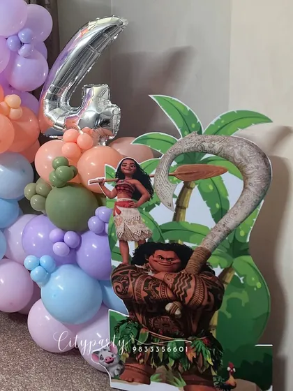 A 'Moana' themed birthday decoration for a 4th birthday. This setup includes character cutouts of Moana and Maui, a large '4' foil balloon, and a tropical-colored balloon garland.