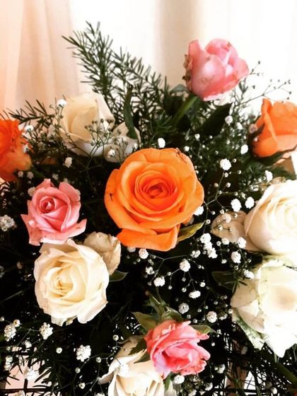 This is a close-up of a bouquet with orange, pink, and white roses. The vibrant colors and fresh greenery add life and beauty to any event space.