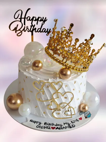 An elegant white and gold birthday cake with a beautiful crown topper. The quilted pattern and heart details add a touch of royalty.