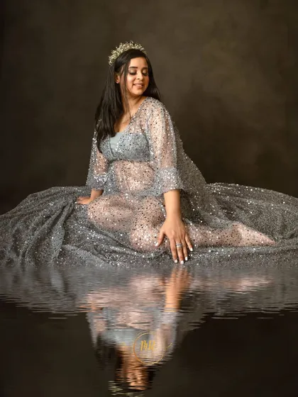 An artistic maternity portrait with a water reflection effect. The mother-to-be is seated in a shimmering silver gown, creating a serene and magical image.