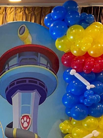 A close-up of a Paw Patrol themed backdrop featuring the iconic Lookout Tower, framed by a primary-colored balloon garland.