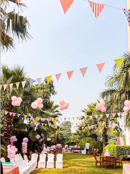 A beautiful outdoor setting for a princess party, with festive bunting and pink balloon clusters hanging among the palm trees, creating a magical, open-air celebration space.
