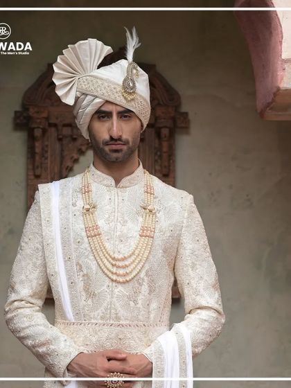 A close-up of a groom in a white sherwani from the Shauhar collection. The focus is on the intricate embroidery and the elegant pearl necklace, details that define luxury.