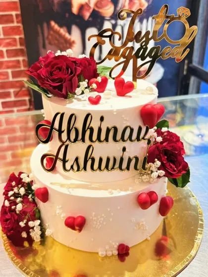 A two-tier engagement cake personalized with the couple's names and decorated with fresh red roses and edible hearts.