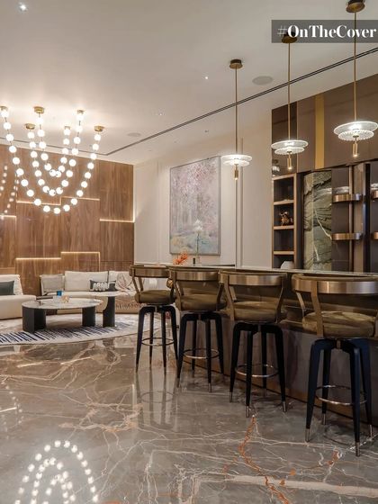 This entertainment area features a sophisticated bar with elegant seating, set against a backdrop of rich wood paneling and intricate lighting. The veined marble floor adds a layer of opulence, making it a perfect space for hosting.