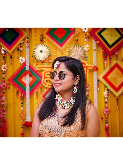 The bride looking cool and chic in sunglasses against the colorful backdrop of her haldi decor.