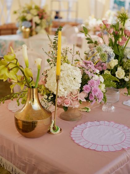 A vibrant centerpiece featuring a mix of colorful flowers in a copper vase, set on a pink tablecloth.