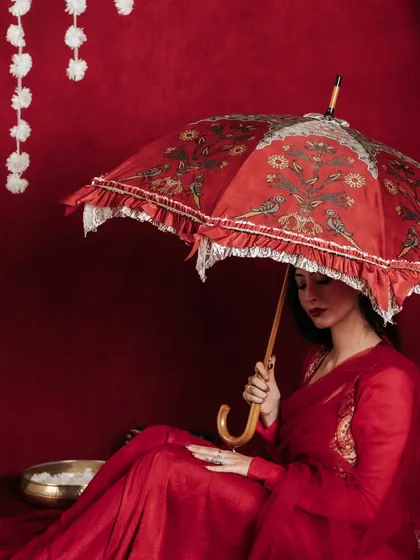 This seated pose offers a different perspective, showing how the umbrella can be used as a prop in various lifestyle scenarios. The composition is quiet and contemplative, focusing on the product's beautiful bird and floral motif.